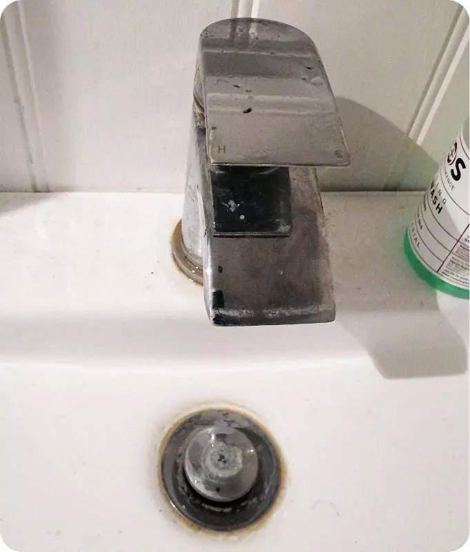 Heavily stained faucet and sink trap before cleaning